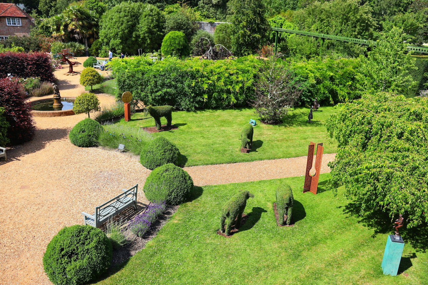 Zielony ogród z topiary w kształcie zwierząt i abstrakcyjnymi rzeźbami.